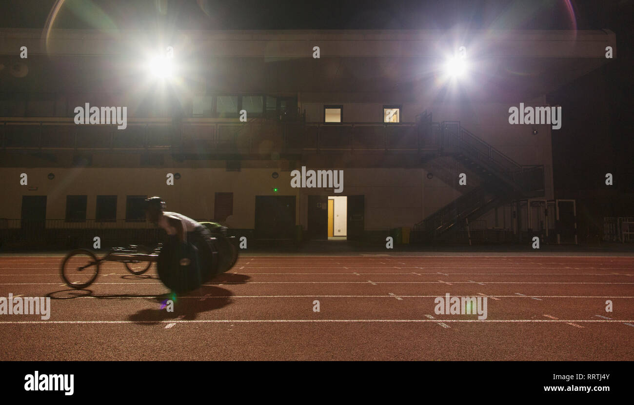 Männlichen querschnittsgelähmten Athlet Training für Rollstuhl Rennen am Sportplatz in der Nacht Stockfoto