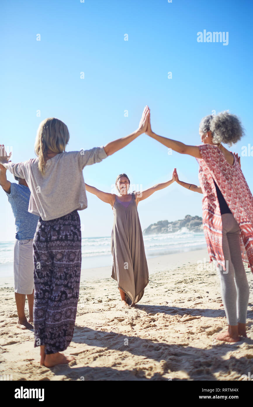Gruppe Hand in Hand im Kreis an sonnigen Strand während Yoga Retreat Stockfoto
