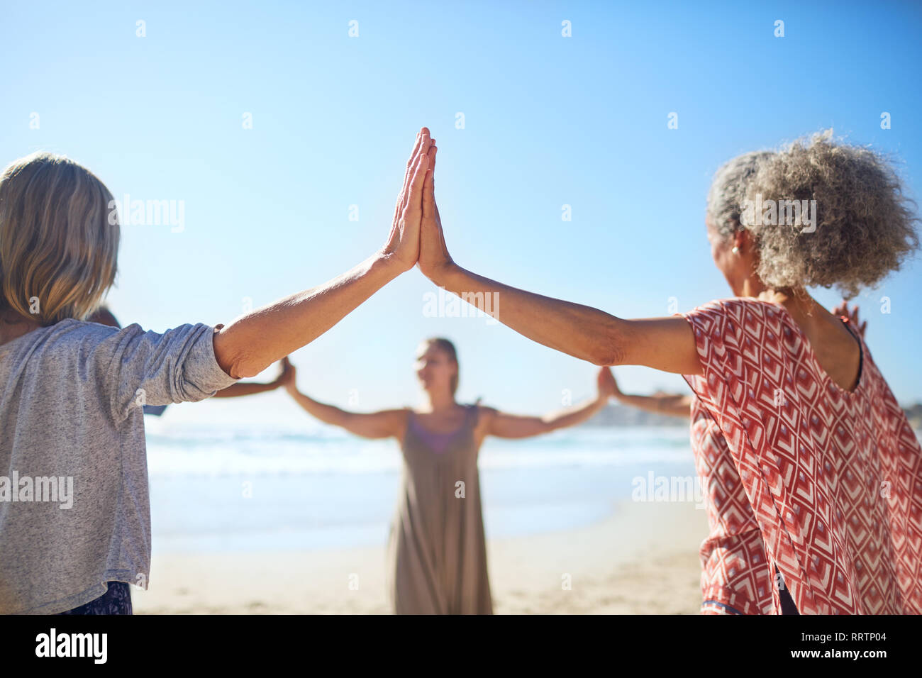Frauen Hand in Hand im Kreis an sonnigen Strand während Yoga Retreat Stockfoto