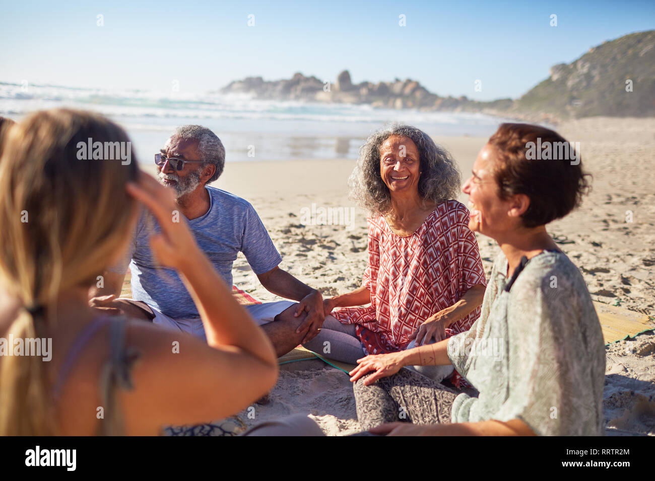 Freunde im Kreis sitzen auf sonnigen Strand während Yoga Retreat Stockfoto