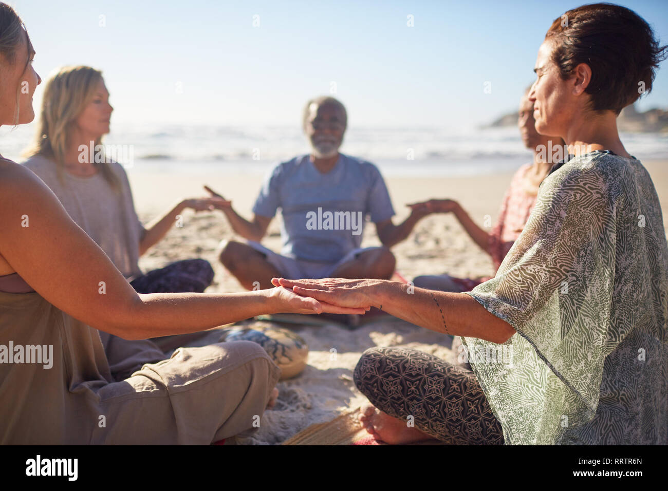 Heitere Menschen meditieren im Kreis an sonnigen Strand während Yoga Retreat Stockfoto