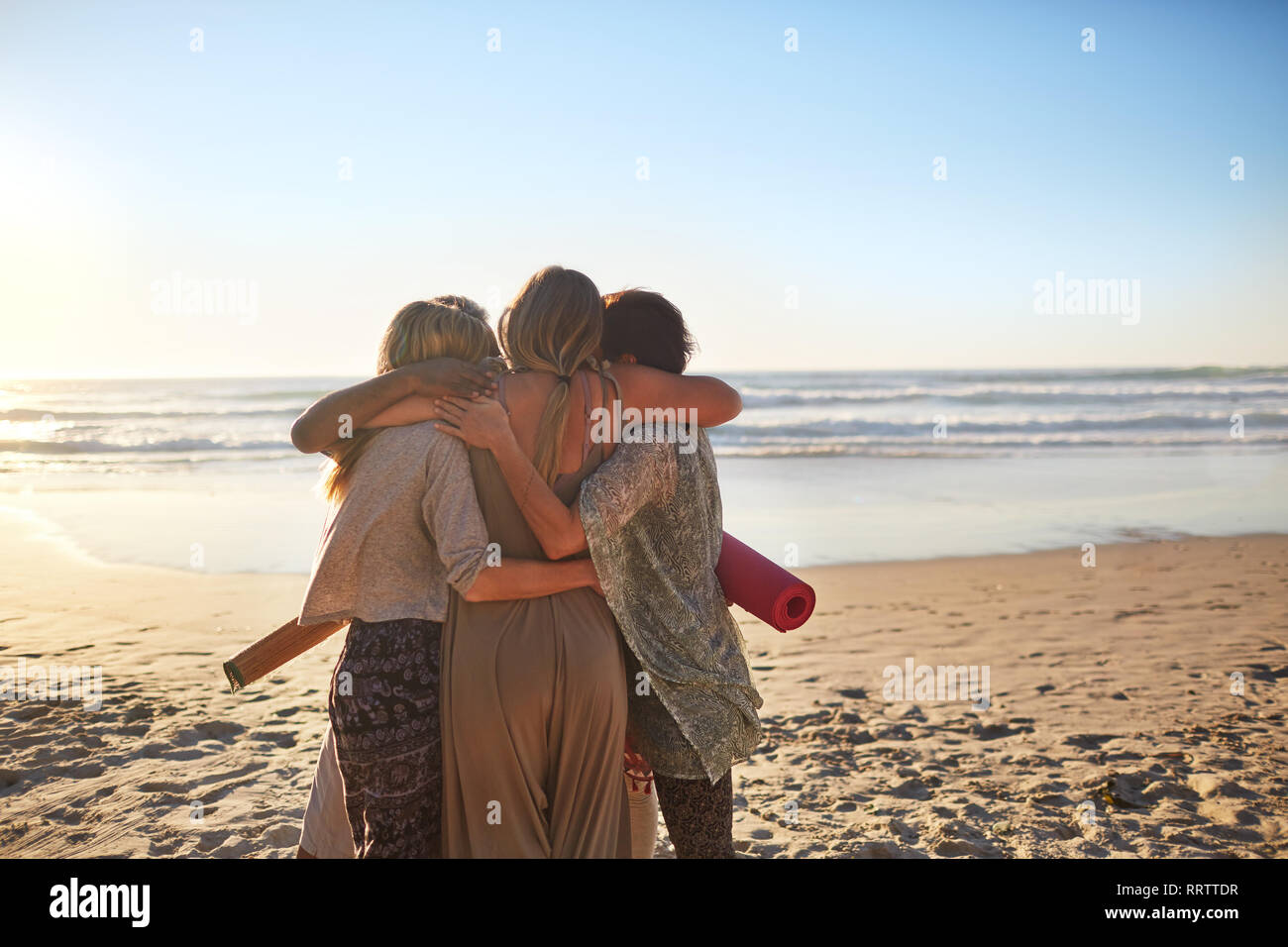 Weibliche Freunde mit Yogamatten umarmen auf Sunny Beach Stockfoto