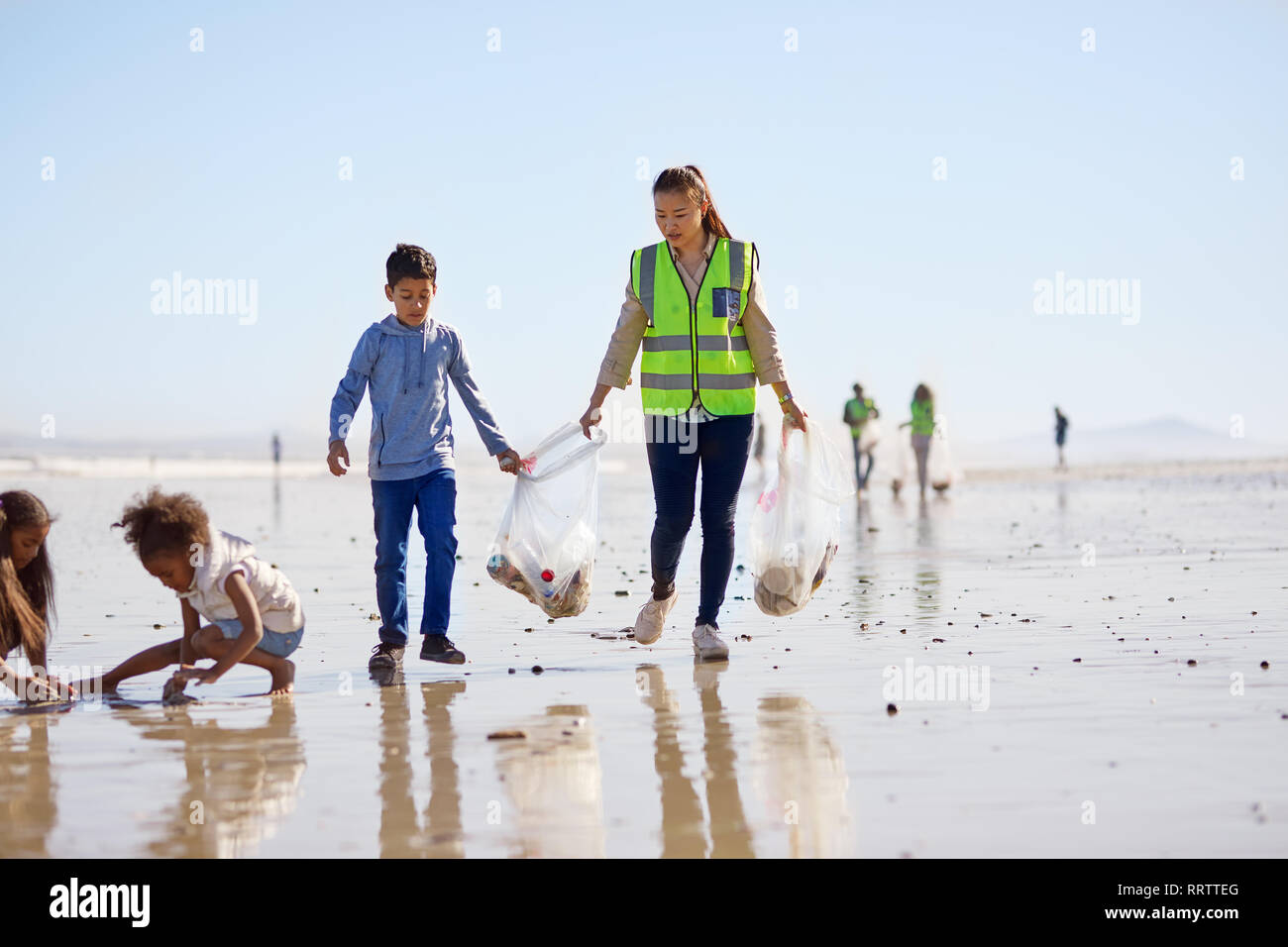 Mutter und Sohn freiwillige Reinigung Wurf auf sonnigen feuchten Sand Strand Stockfoto