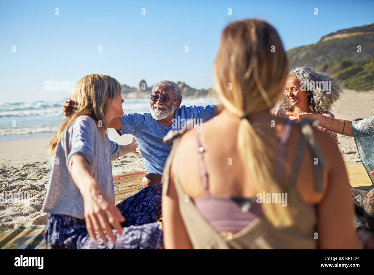 Freunde umarmen im Kreis an sonnigen Strand während Yoga Retreat Stockfoto