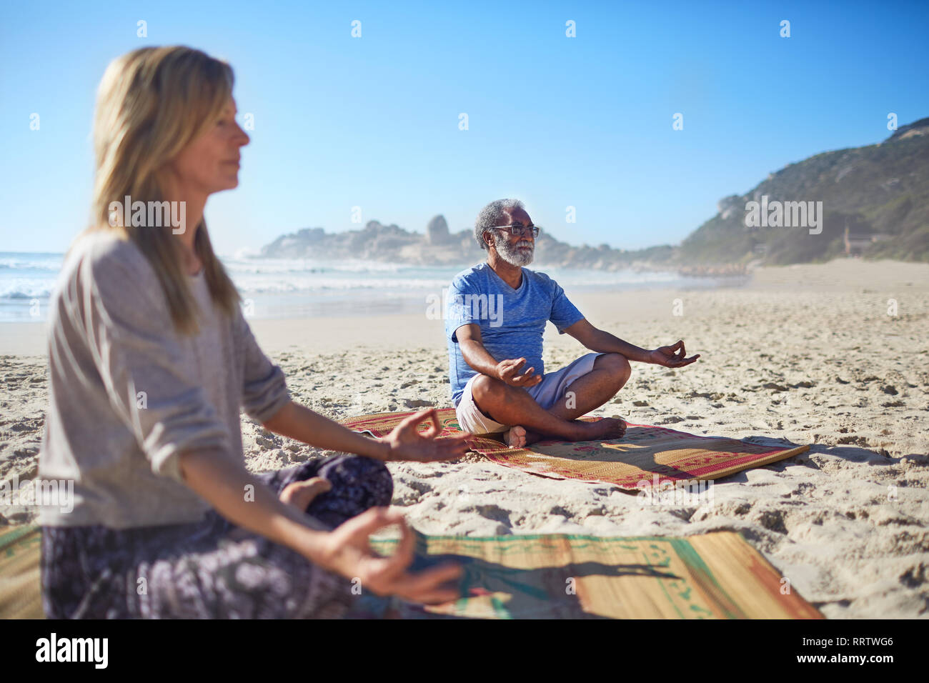Heitere Menschen meditieren auf sonnigen Strand während Yoga Retreat Stockfoto