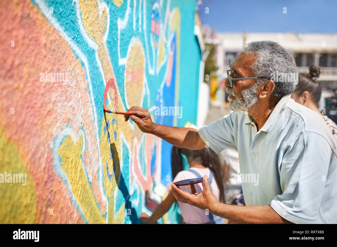 Ältere männliche Freiwillige Malerei lebendige Wandbild an sonnigen Wand Stockfoto