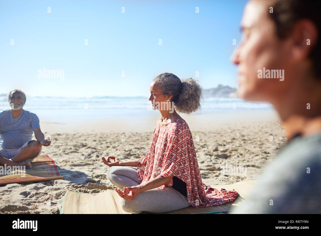 Serene senior Frau meditieren auf sonnigen Strand während Yoga Retreat Stockfoto