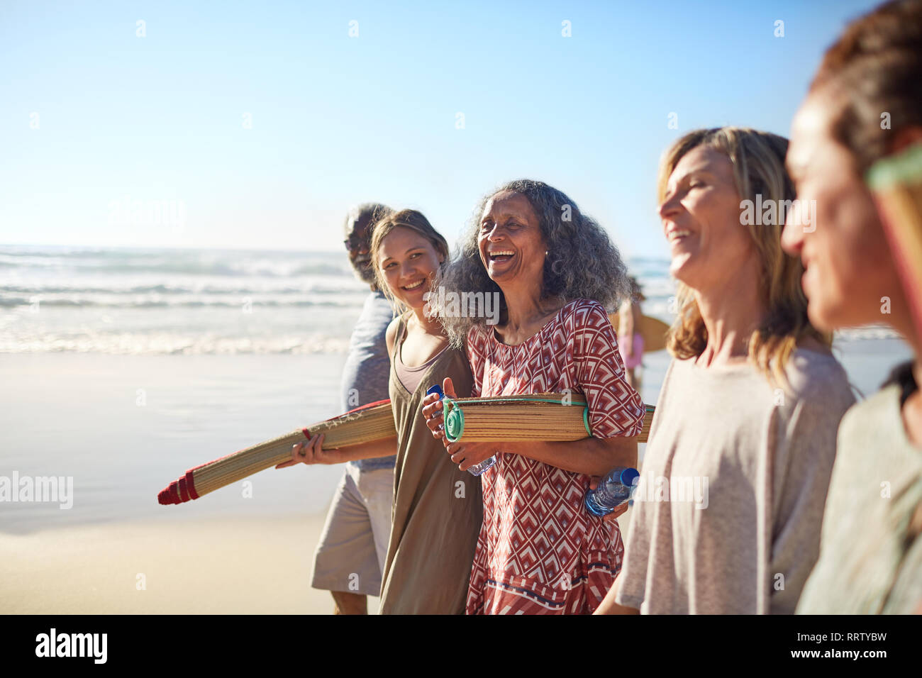 Gerne Freunde mit yogamatten an sonnigen Strand während Yoga Retreat Stockfoto