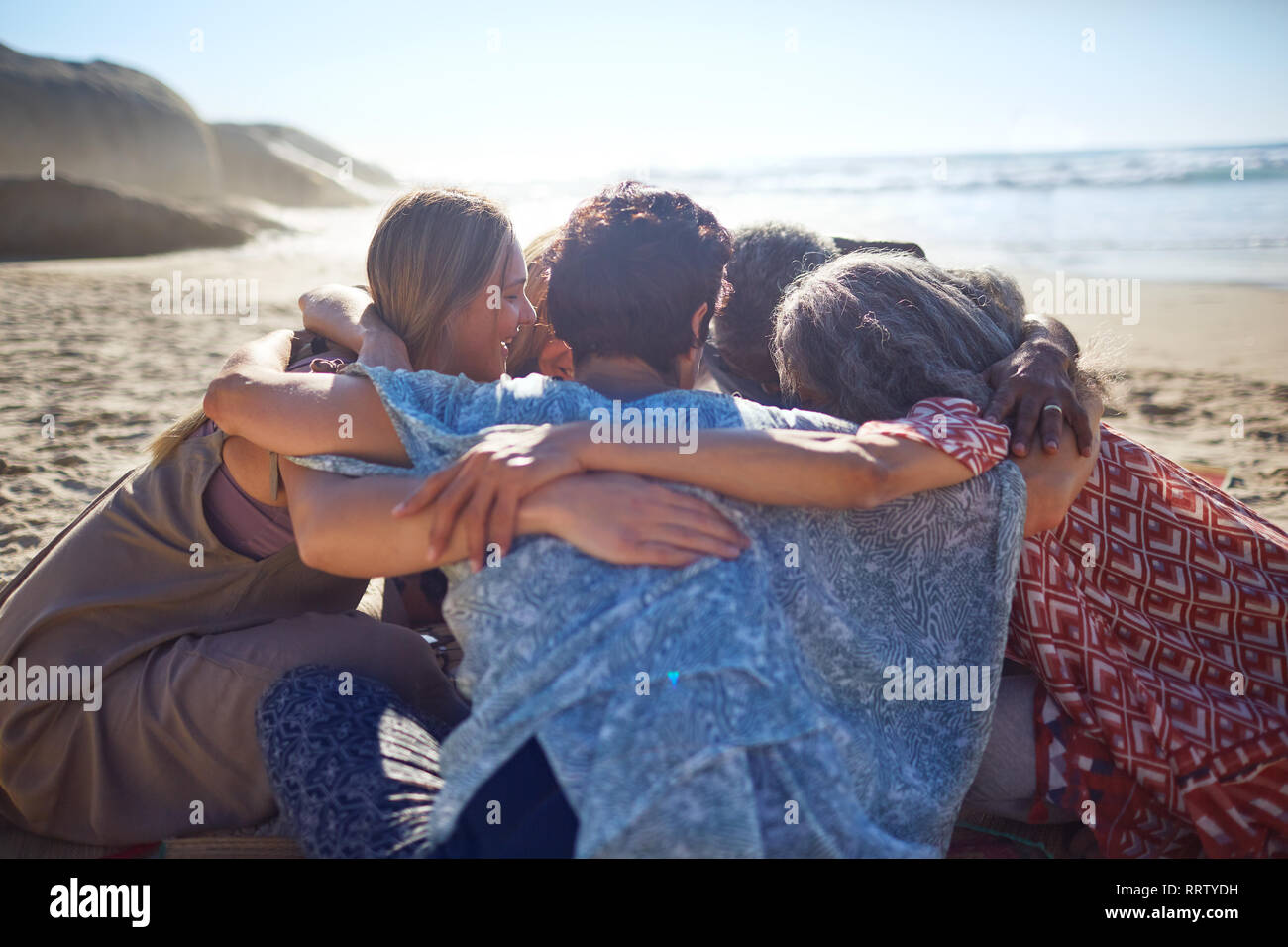 Gruppe umarmen im Kreis an sonnigen Strand während Yoga Retreat Stockfoto