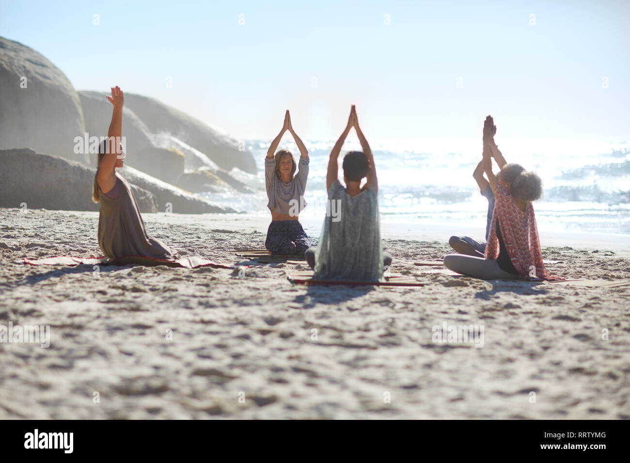 Heitere Menschen im Kreis meditieren auf sonnigen Strand während Yoga Retreat Stockfoto