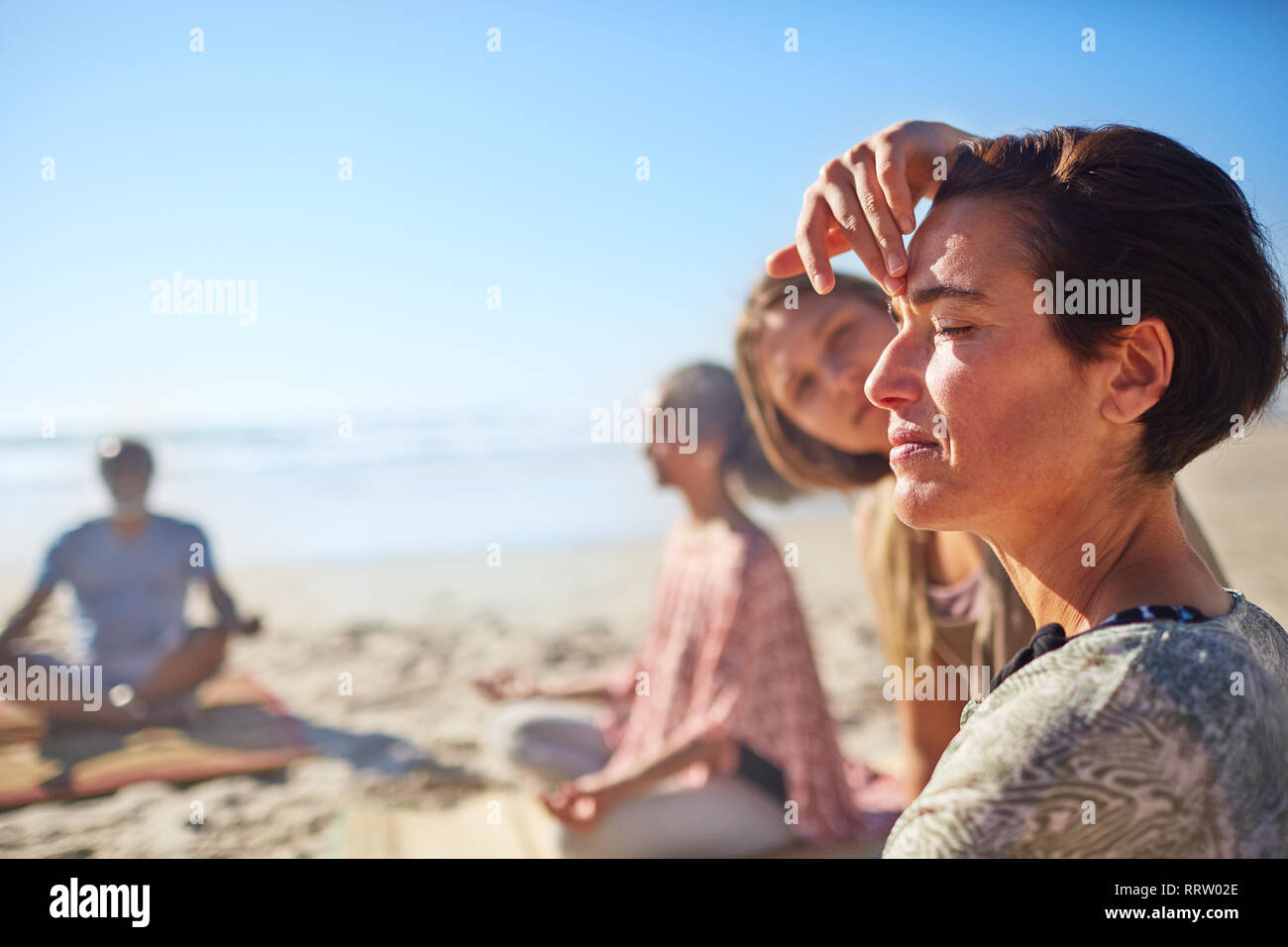 Yoga Instructor berühren drittes Auge der Frau meditieren auf sonnigen Strand während Yoga Retreat Stockfoto