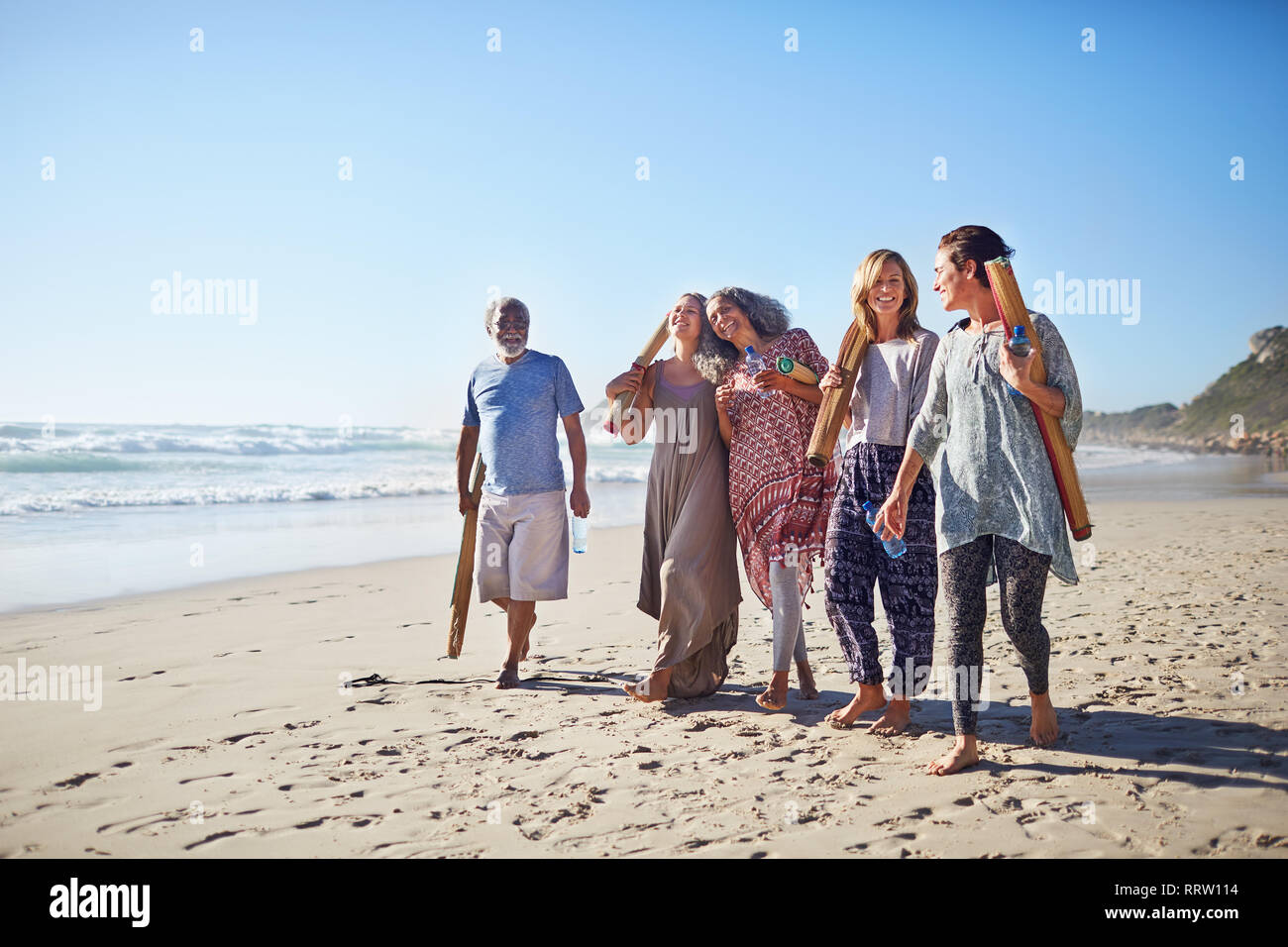 Freunde gehen mit yogamatten an sonnigen Strand während Yoga Retreat Stockfoto