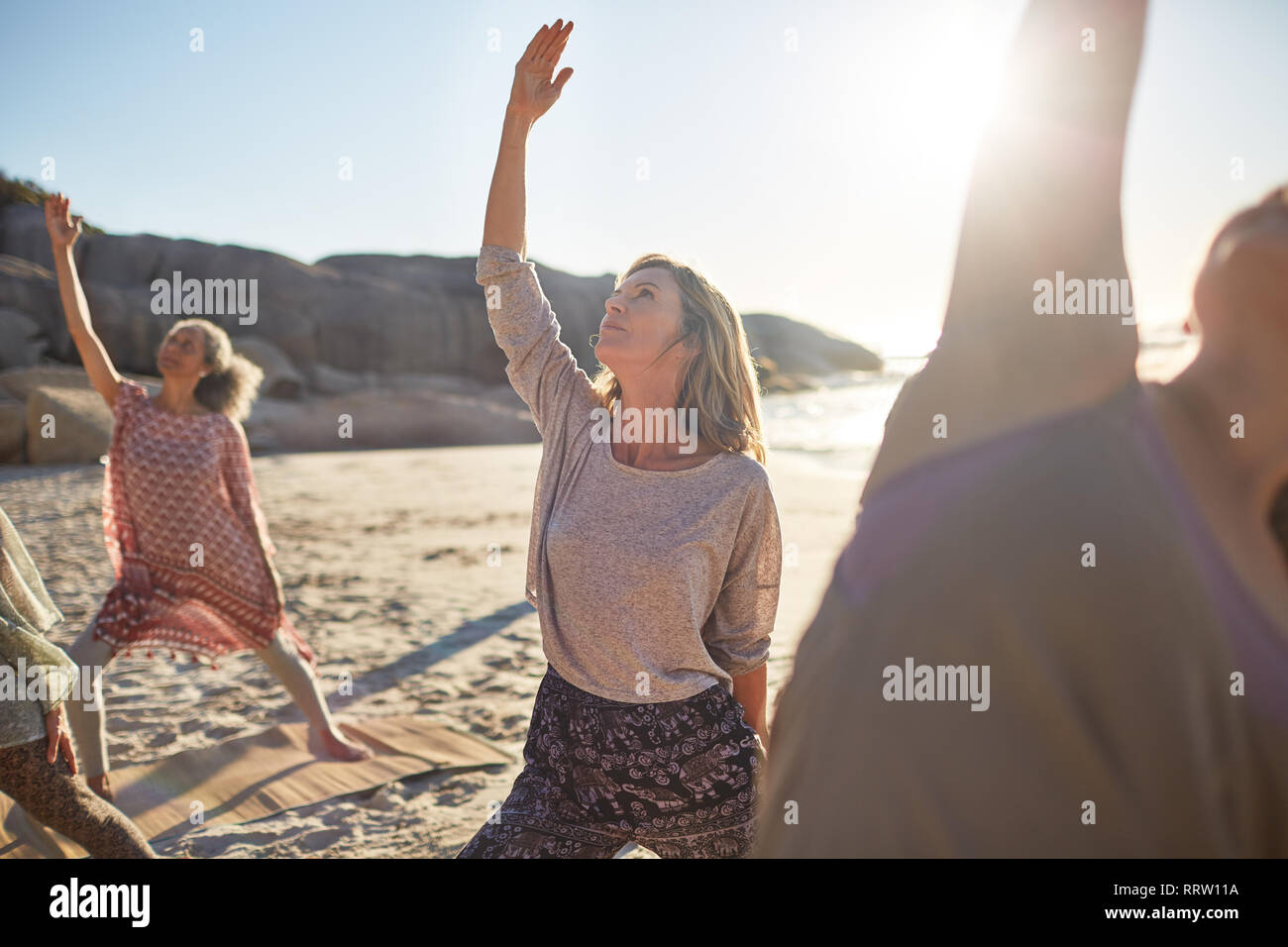Heitere Frau üben Reverse warrior Pose an sonnigen Strand während Yoga Retreat Stockfoto