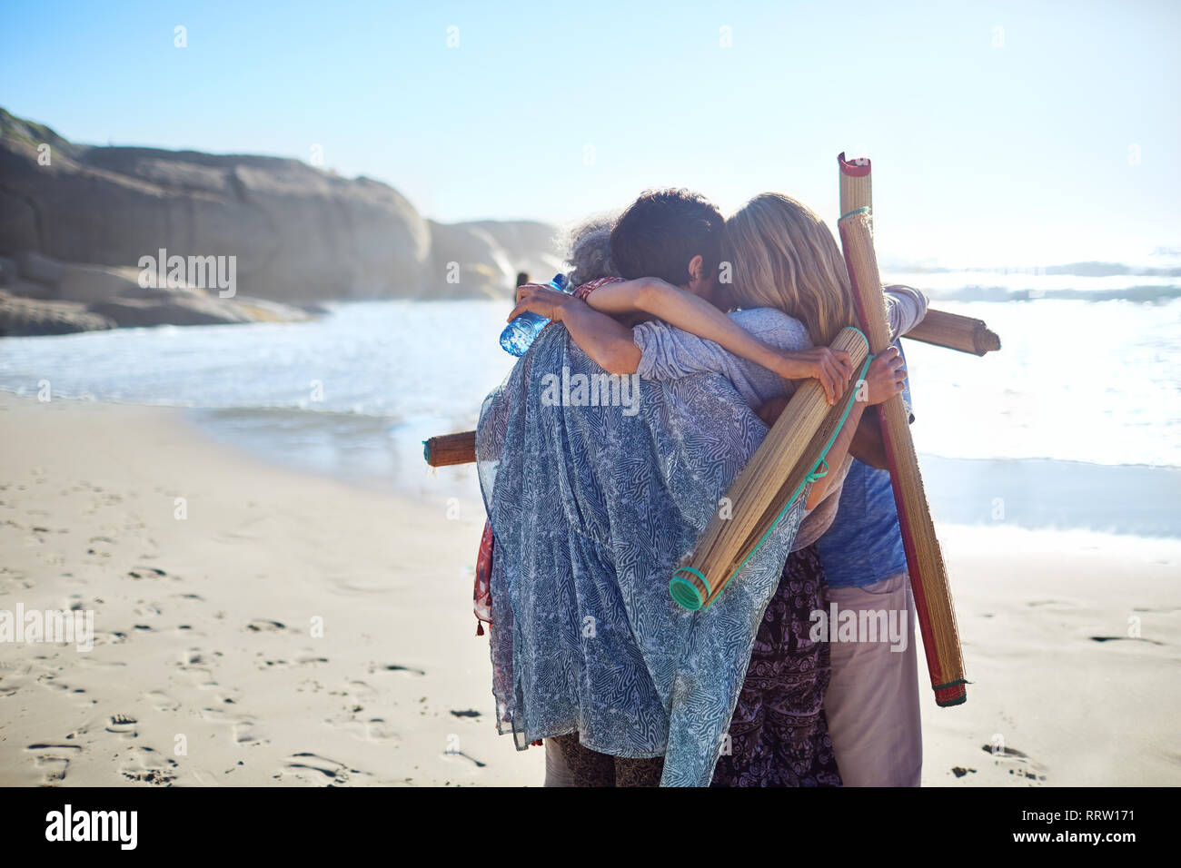 Frauen Freunde mit Yogamatten umarmen an sonnigen Strand während Yoga Retreat Stockfoto