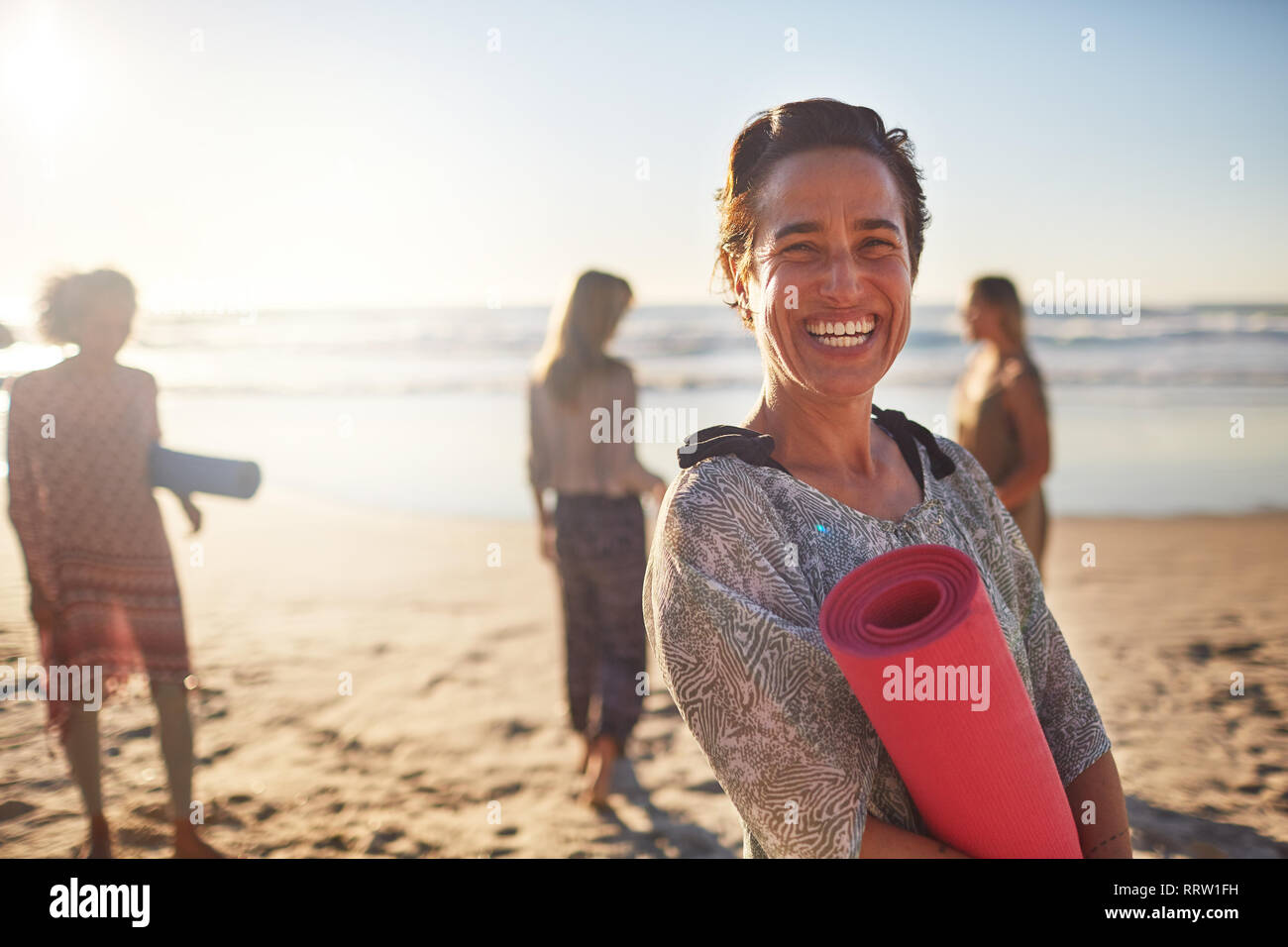 Porträt Frau mit Yoga Matte auf sonnigen Strand während Yoga Retreat Stockfoto