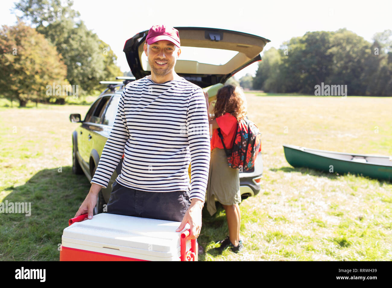 Portrait lächelnden Mann camping Kühler, entladen Auto im sonnigen Bereich Stockfoto