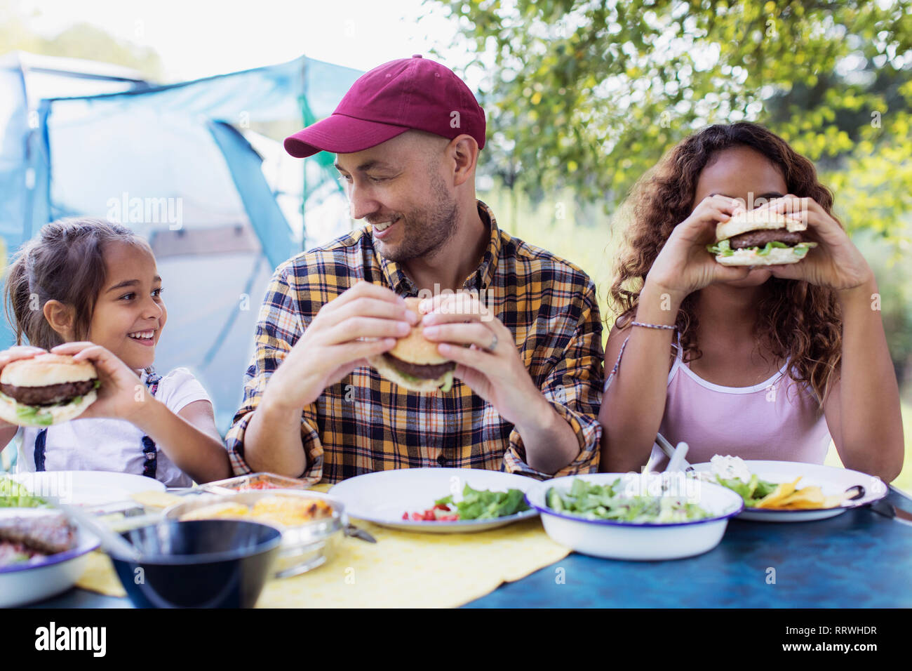 Gerne Vater und Töchter essen Grill Hamburger auf dem Campingplatz Stockfoto