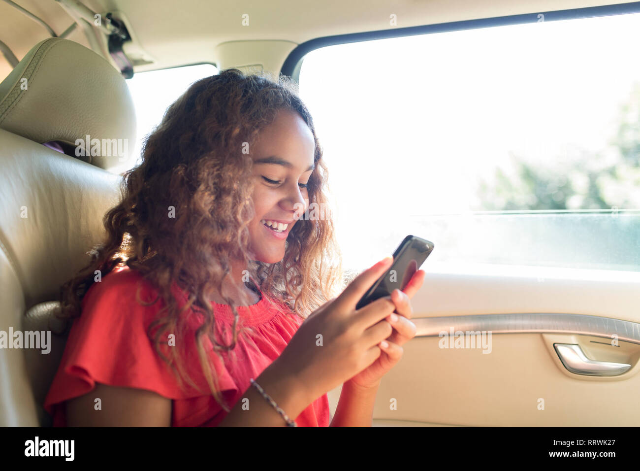 Lächelnd tween Mädchen mit Smart Phone in der Rücksitz des Autos Stockfoto