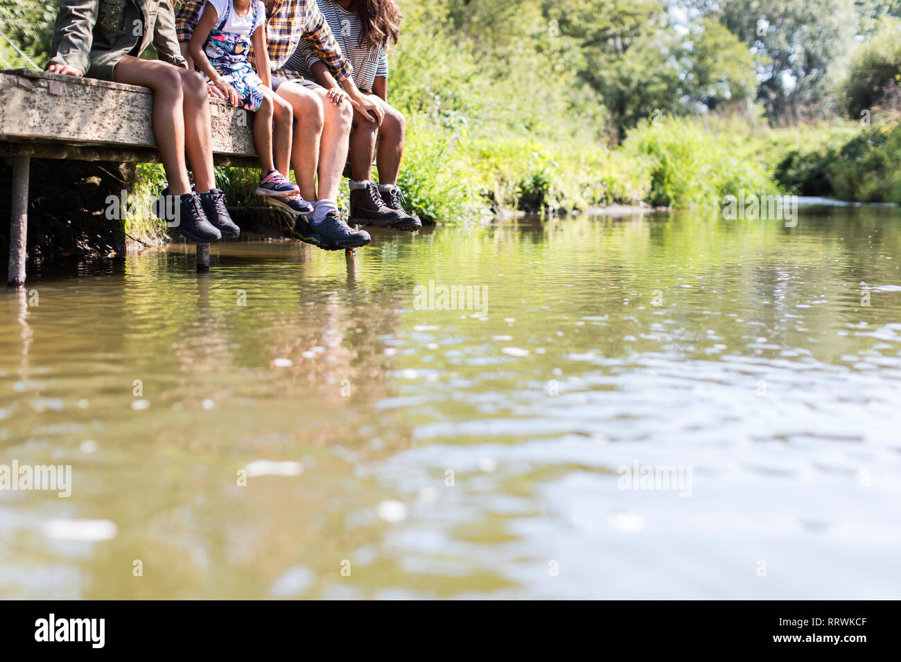 Familie baumelnden Füßen aus sonnigen Riverside dock Stockfoto