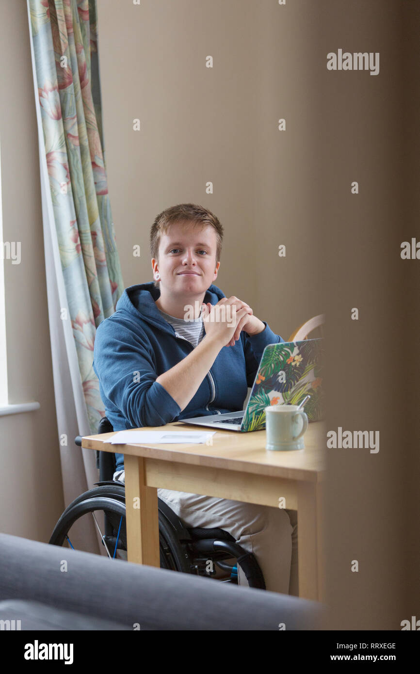 Portrait selbstbewussten jungen Frau im Rollstuhl mit Laptop am Esstisch Stockfoto