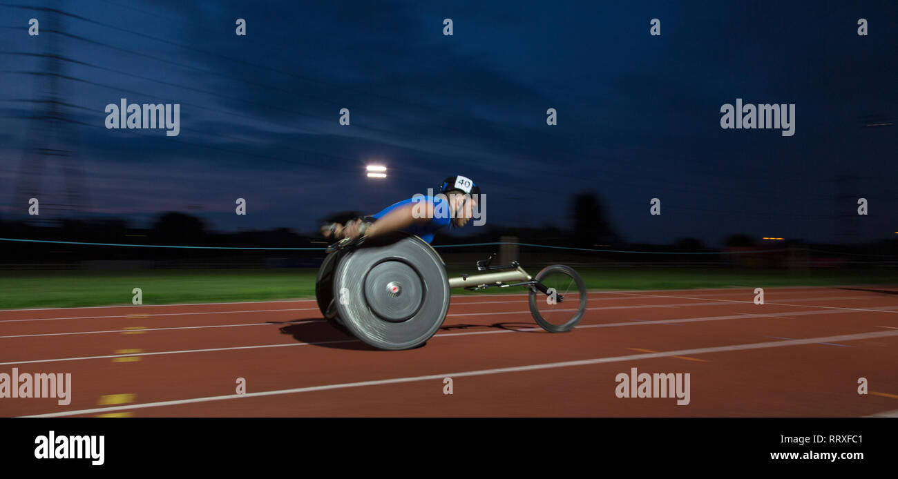 Jungen männlichen querschnittsgelähmten Athlet Beschleunigung zusammen Sport Track im Rollstuhl Rennen bei Nacht Stockfoto