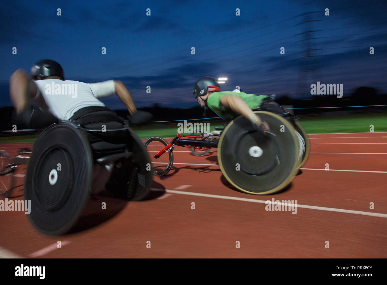Querschnittsgelähmte Sportler Beschleunigung zusammen Sport Spur während der Rollstuhl Rennen bei Nacht Stockfoto
