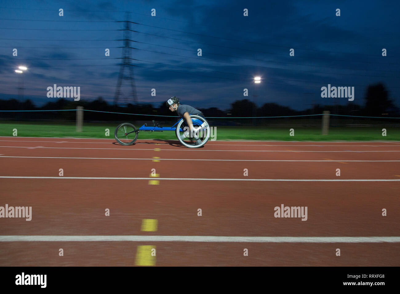 Junge weibliche paraplegic Athlet Beschleunigung zusammen Sport Track im Rollstuhl Rennen bei Nacht Stockfoto