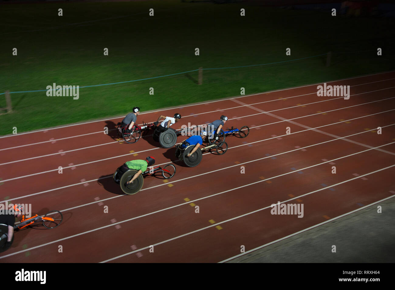 Querschnittsgelähmte Sportler Beschleunigung zusammen Sport Track im Rollstuhl Rennen bei Nacht Stockfoto