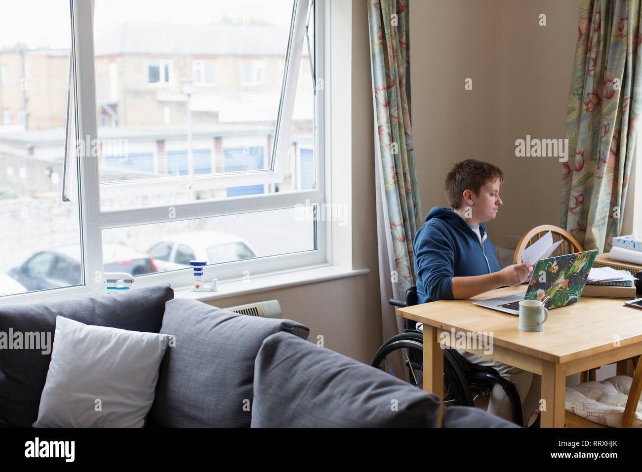 Junge Frauen im Rollstuhl mit Laptop am Esstisch Stockfoto