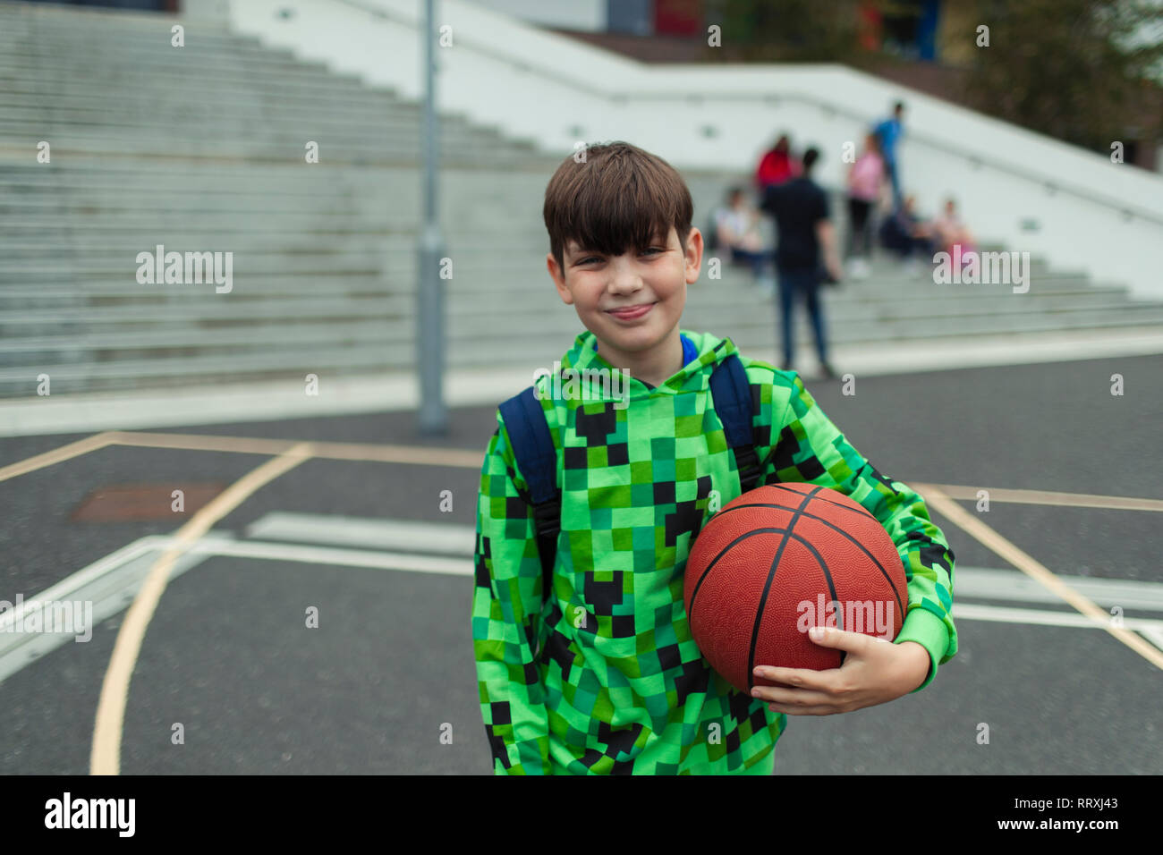 Portrait zuversichtlich tween Junge mit Basketball in Schulhof Stockfoto