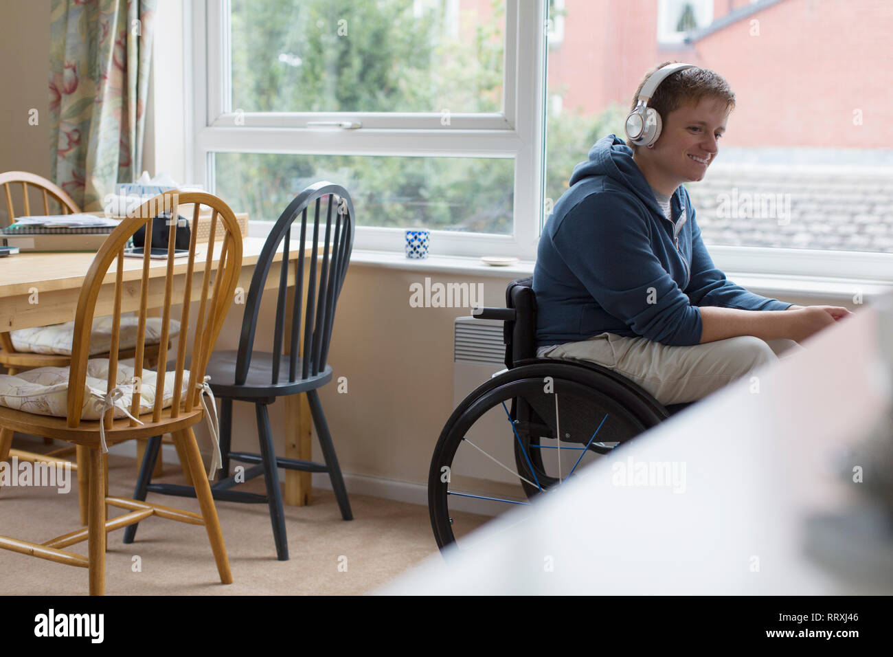Junge Frau im Rollstuhl Musikhören mit Kopfhörern mit Fenster Stockfoto