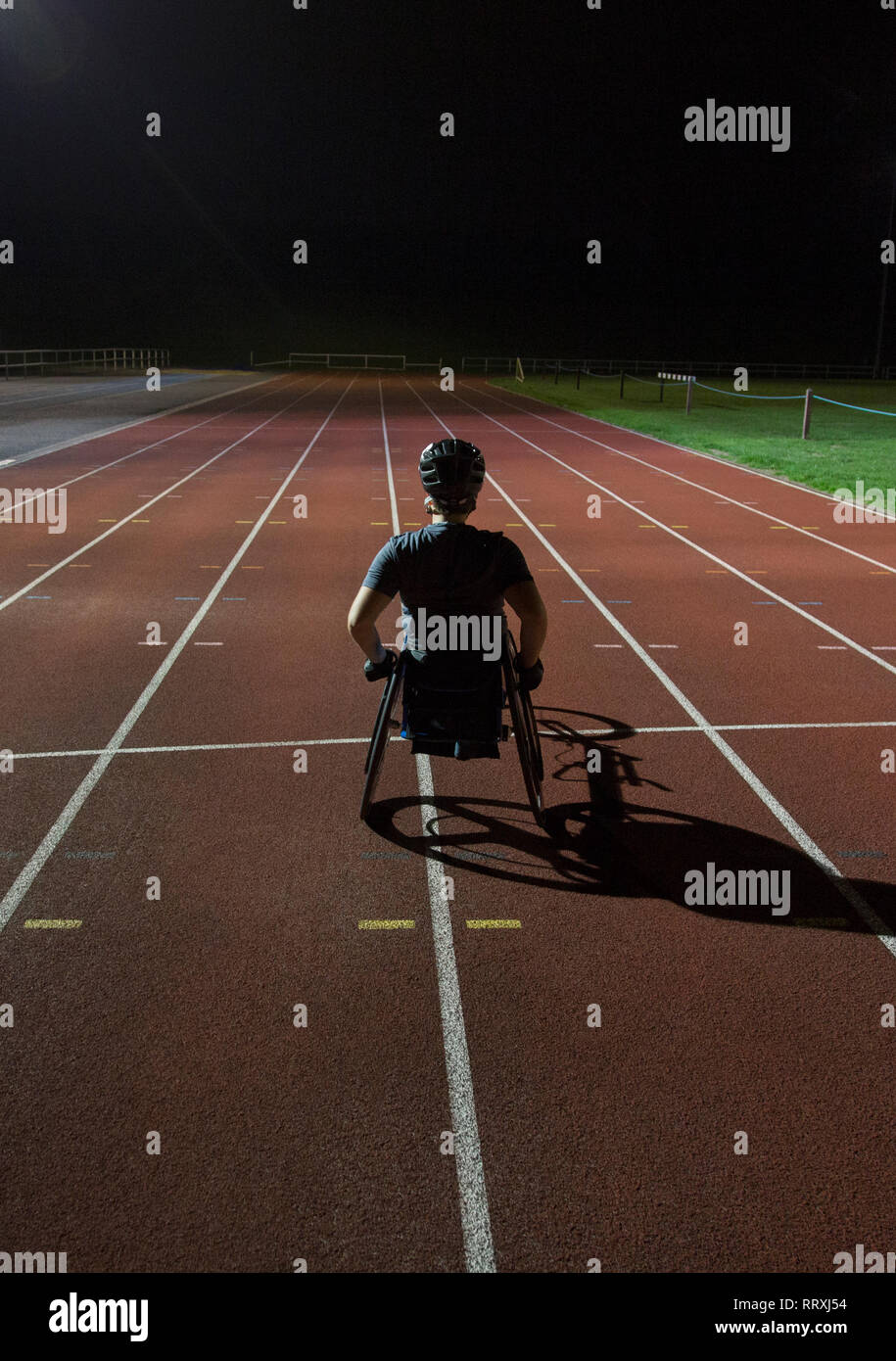 Entschlossene junge weibliche paraplegic Athlet Training für Rollstuhl Rennen am Sportplatz in der Nacht Stockfoto