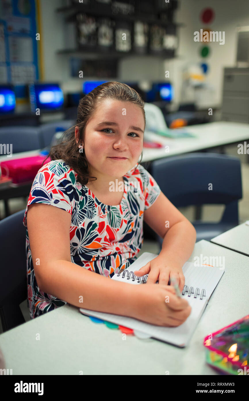 Porträt Lächeln, zuversichtlich Junior high school Mädchen schreiben in Notebook im Klassenzimmer Stockfoto