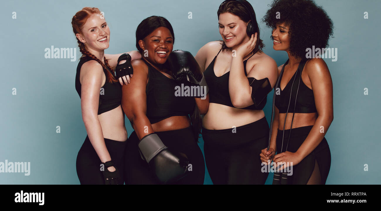Gruppe von Frauen unterschiedlicher Rasse und Größe in Sportkleidung ständigen zusammen. Diverse Frauen mit sportgeräte an Kamera gegen Grau bac suchen Stockfoto