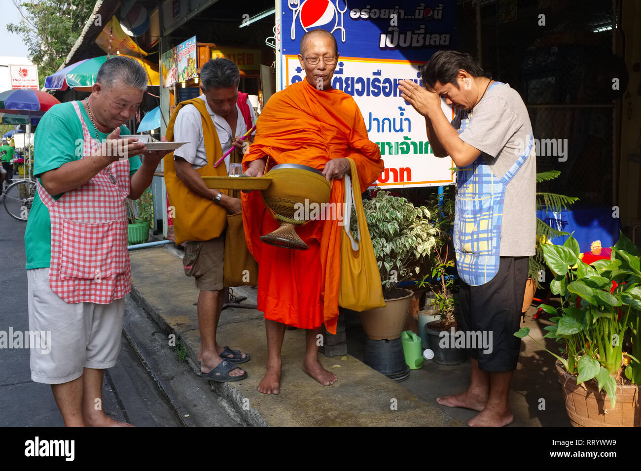 Lokale Ladenbesitzer in Thonburi, Bangkok, Thailand, einen buddhistischen Mönch während seiner traditionellen morgendlichen Gebet, Almosen Runde Stockfoto