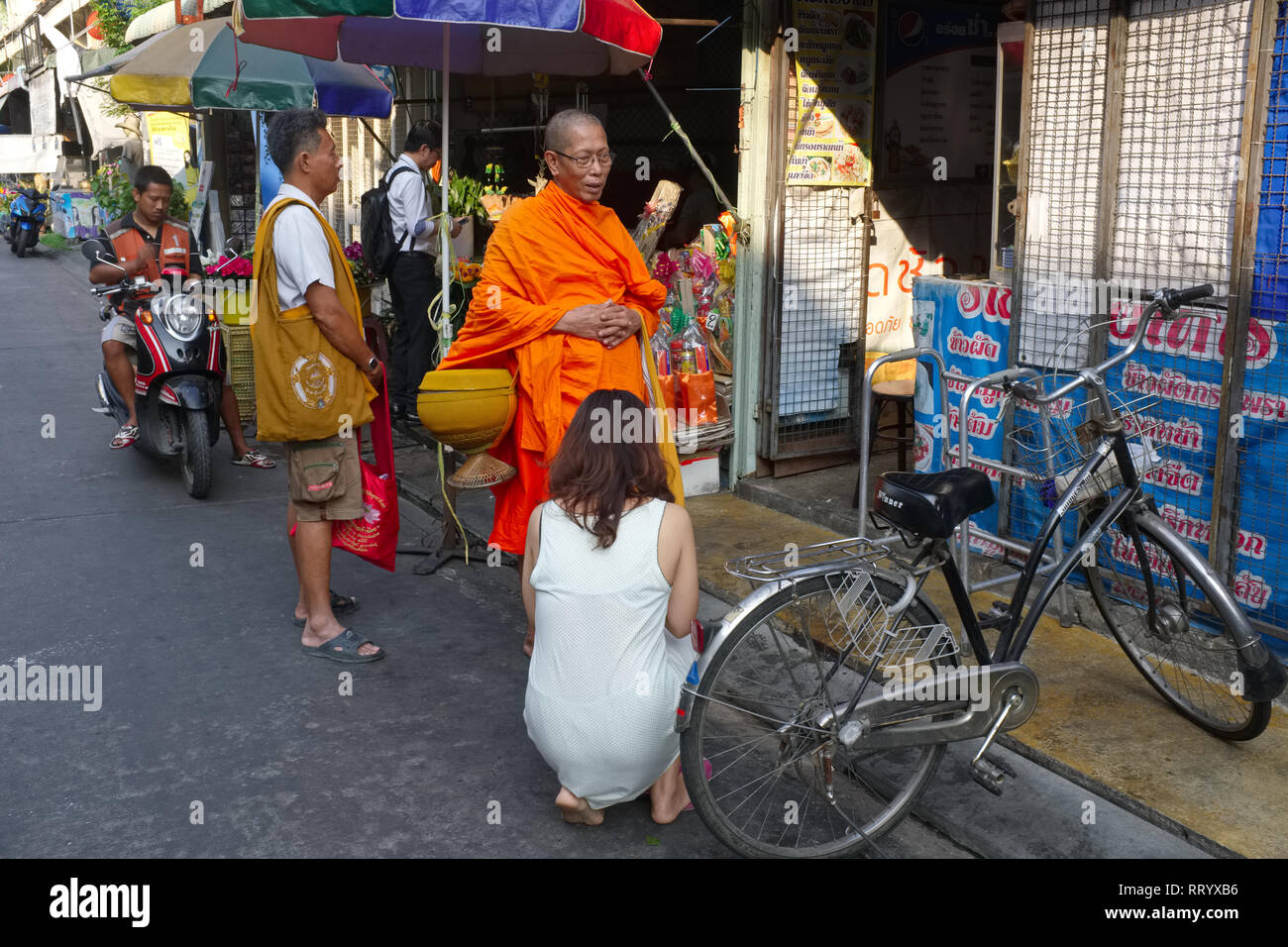 Eine Frau in Thonburi, Bangkok, Thailand, kniend und betend vor ein buddhistischer Mönch während seiner traditionellen morgendlichen Runde Almosen. Stockfoto