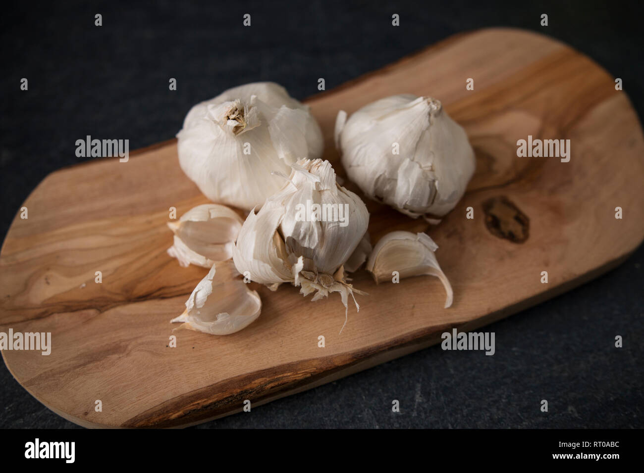 Drei Köpfe von Knoblauch (Allium sativum) auf einem Schneidebrett aus Olivenholz. Stockfoto
