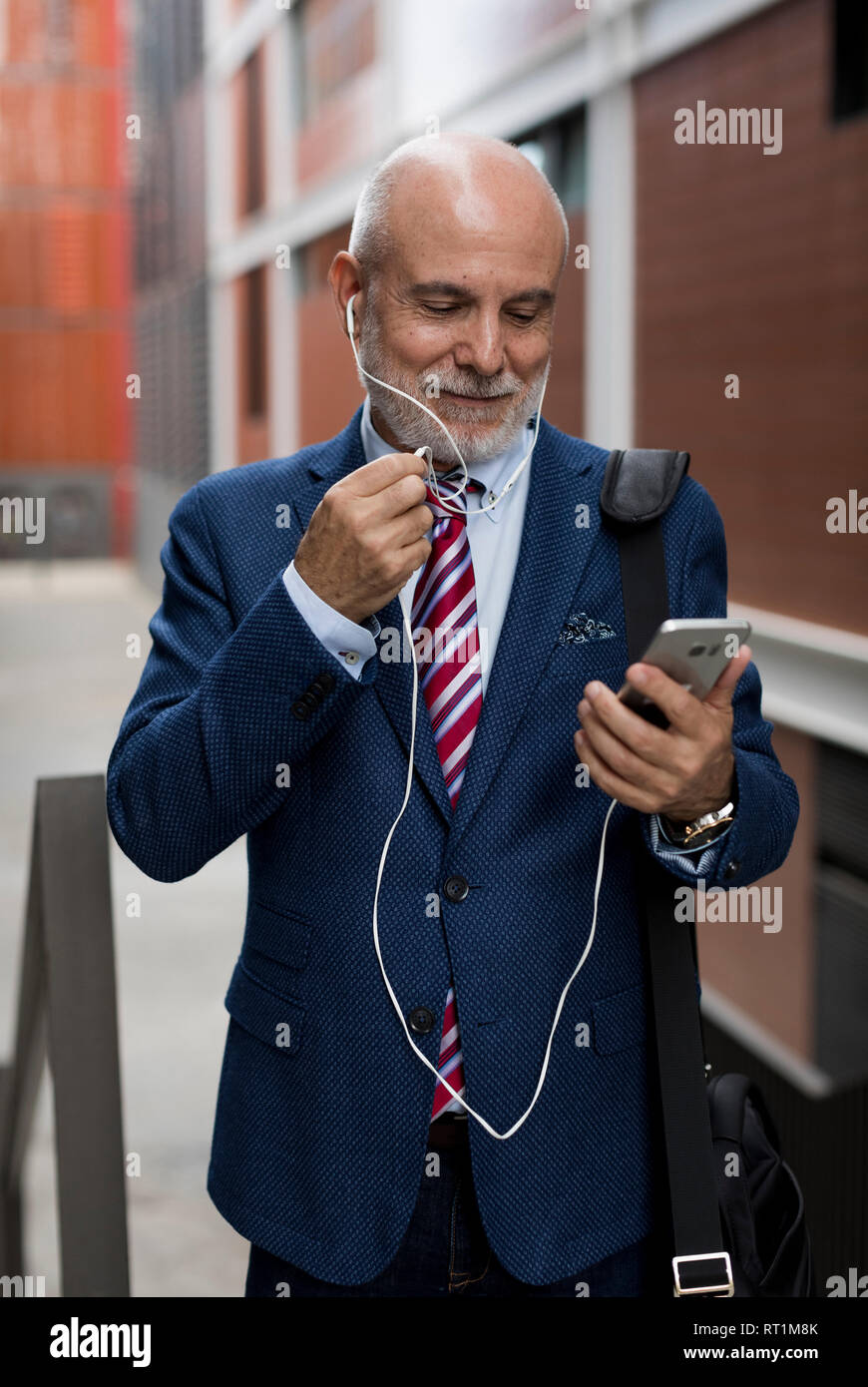 Senior Geschäftsmann mit Mobiltelefon- und Ohrhörer im Freien Stockfoto
