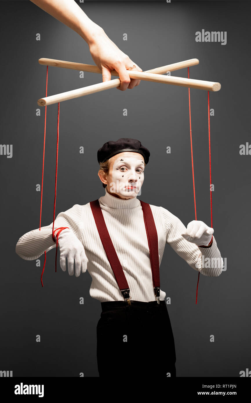 Schauspieler wie eine Marionette mit Seilen von einer riesigen Hand gesteuert auf dem grauen Hintergrund. Konzept der menschlichen Steuerung Stockfoto