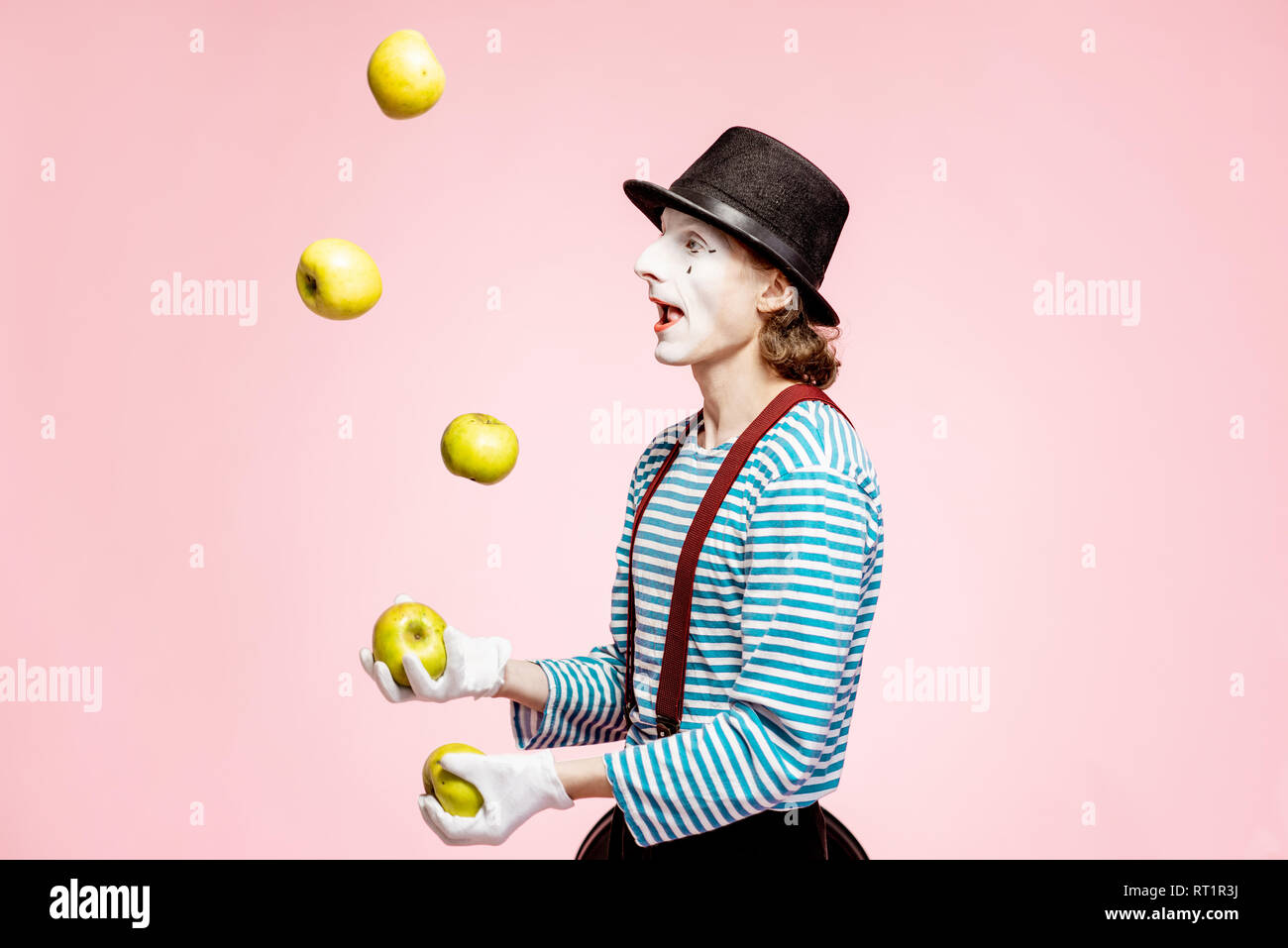 Pantomime mit weißem Gesicht Make-up jonglieren mit Äpfeln auf der rosa Hintergrund im Studio Stockfoto