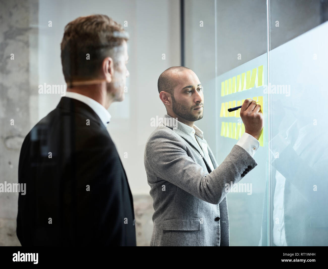 Geschäftsmann an Kollegen schreiben auf Haftnotizen an der Glasscheibe im Büro suchen Stockfoto