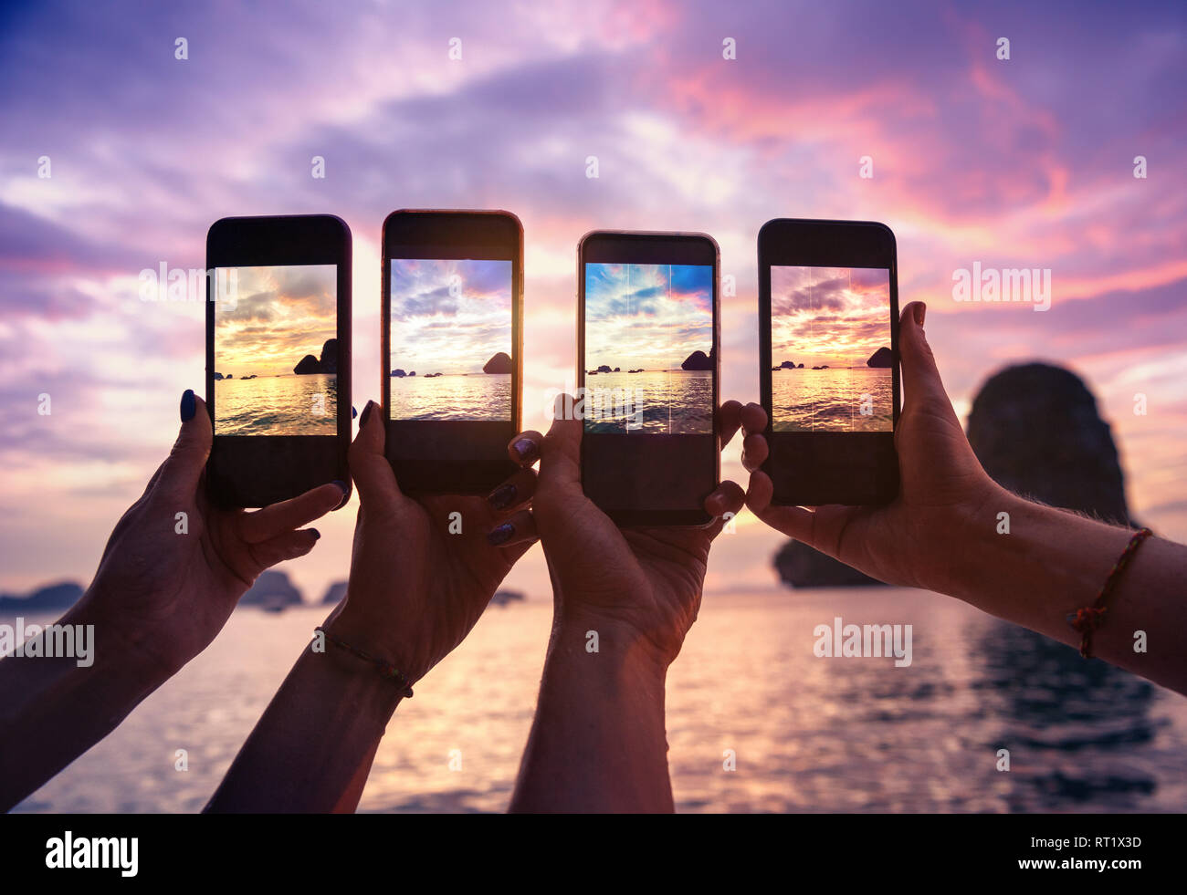 Nahaufnahme von vier Händen mit Mobiltelefonen unter Foto der schönen Sonnenuntergang über dem Meer Stockfoto