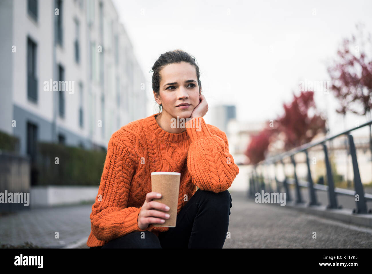 Portrait von nachdenklich Frau mit Kaffee trinken gehen tragen orange Strickpullover im Freien Stockfoto