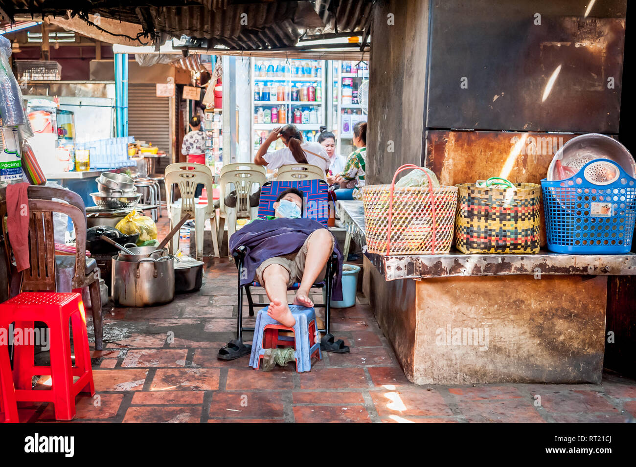 Szenen von einem Indoor-Markt in Phnom Penh, Kambodscha, Südostasien.EIN Marktstallhalter nimmt ein Nickerchen mit einer Gesichtsmaske auf einem beengten Markt. Stockfoto