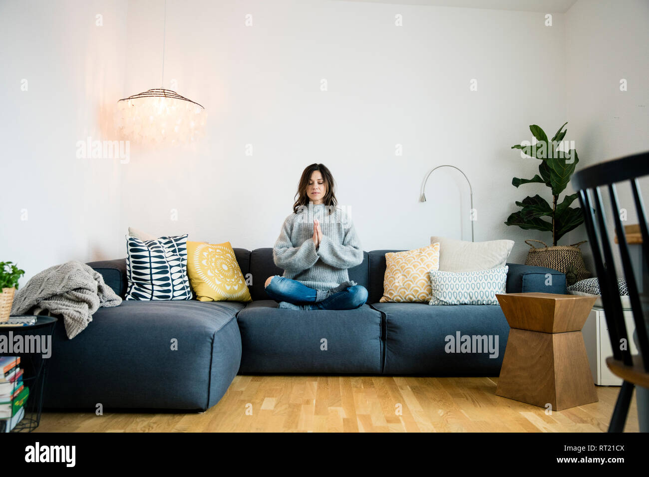 Reife Frau sitzt im Schneidersitz auf der Couch mit geschlossenen Augen, Meditieren zu Hause Stockfoto