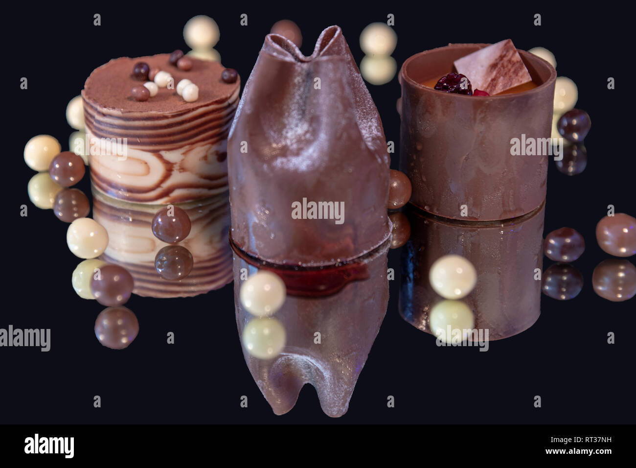 Drei individuelle Schokolade Kuchen auf einen Spiegel mit dunklen Hintergrund mit Schokolade Kugel Stockfoto