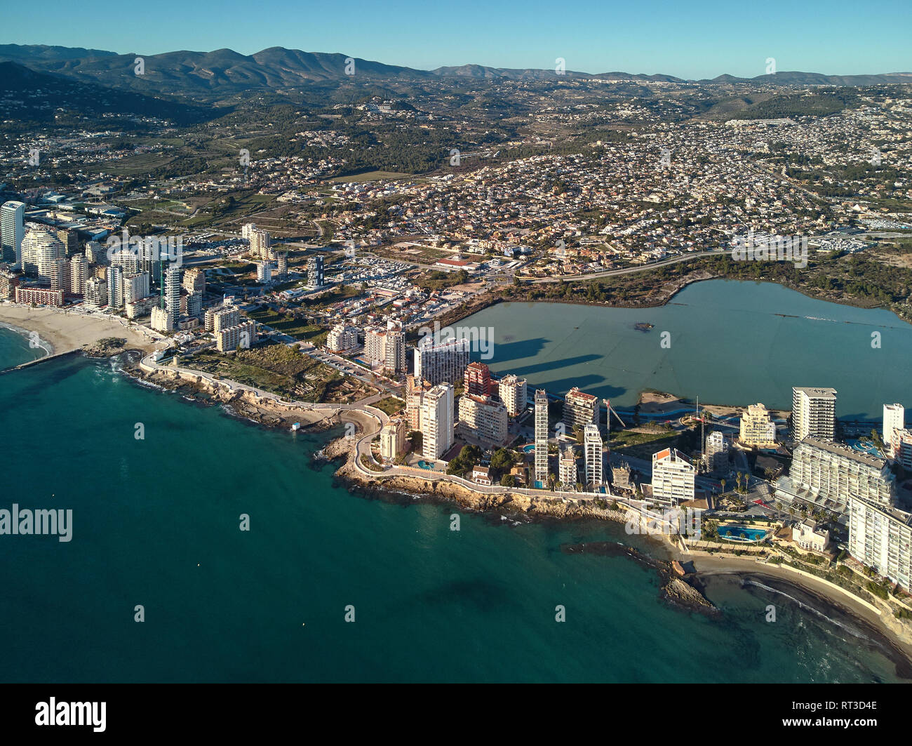 Drone sicht Calpe Landzunge zwischen Meer und See. Stadtbild modernen Wolkenkratzern sonnigen Tag Grün Türkis Wasser Stockfoto