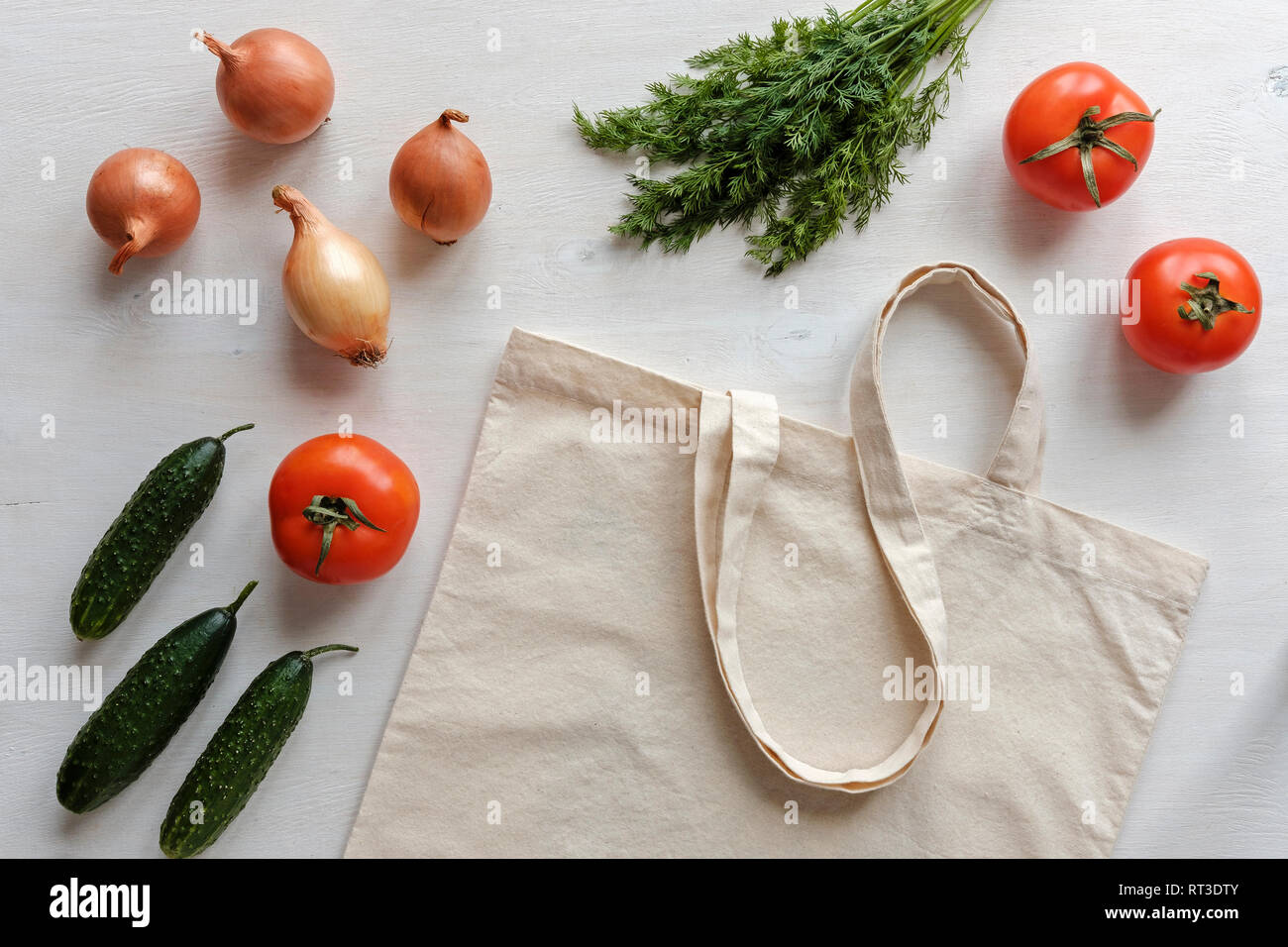 Stoff wieder verwendbare Einkaufstasche mit Lebensmitteln um einschließlich Tomaten, Zwiebeln, Gurken und Greens in einem flachen noch leben verstreut Stockfoto
