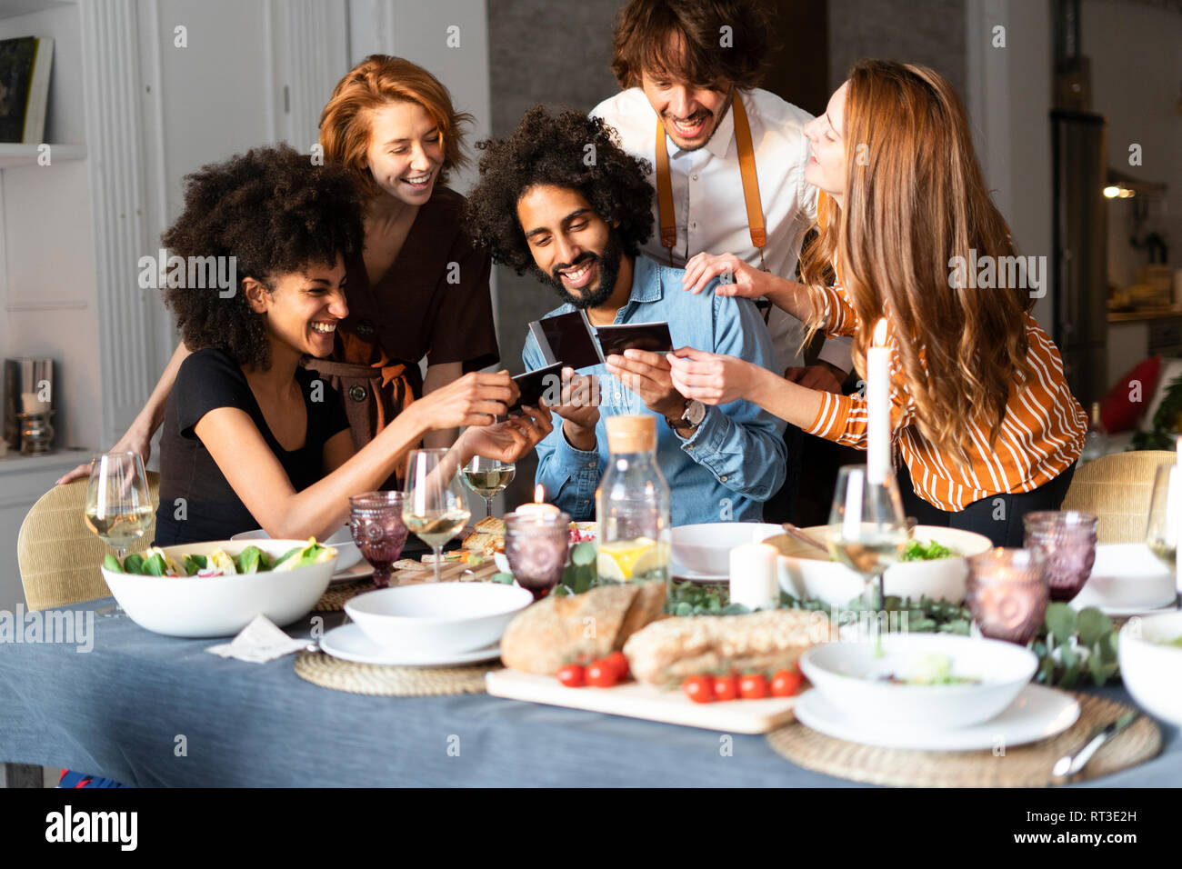 Freunde am Esstisch sitzend, auf Fotos suchen Stockfoto
