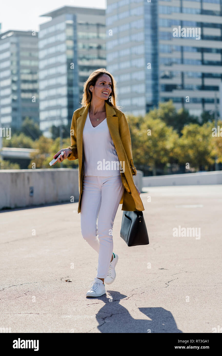 Lächelnde Frau mit Handy und Handtasche in der Stadt unterwegs. Stockfoto